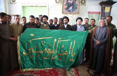 تقديم راية أمير المؤمنين (ع) إلى عائلة الشهيد شيخ المجاهدين في فرقة الإمام علي (ع) التابعة للعتبة العلوية